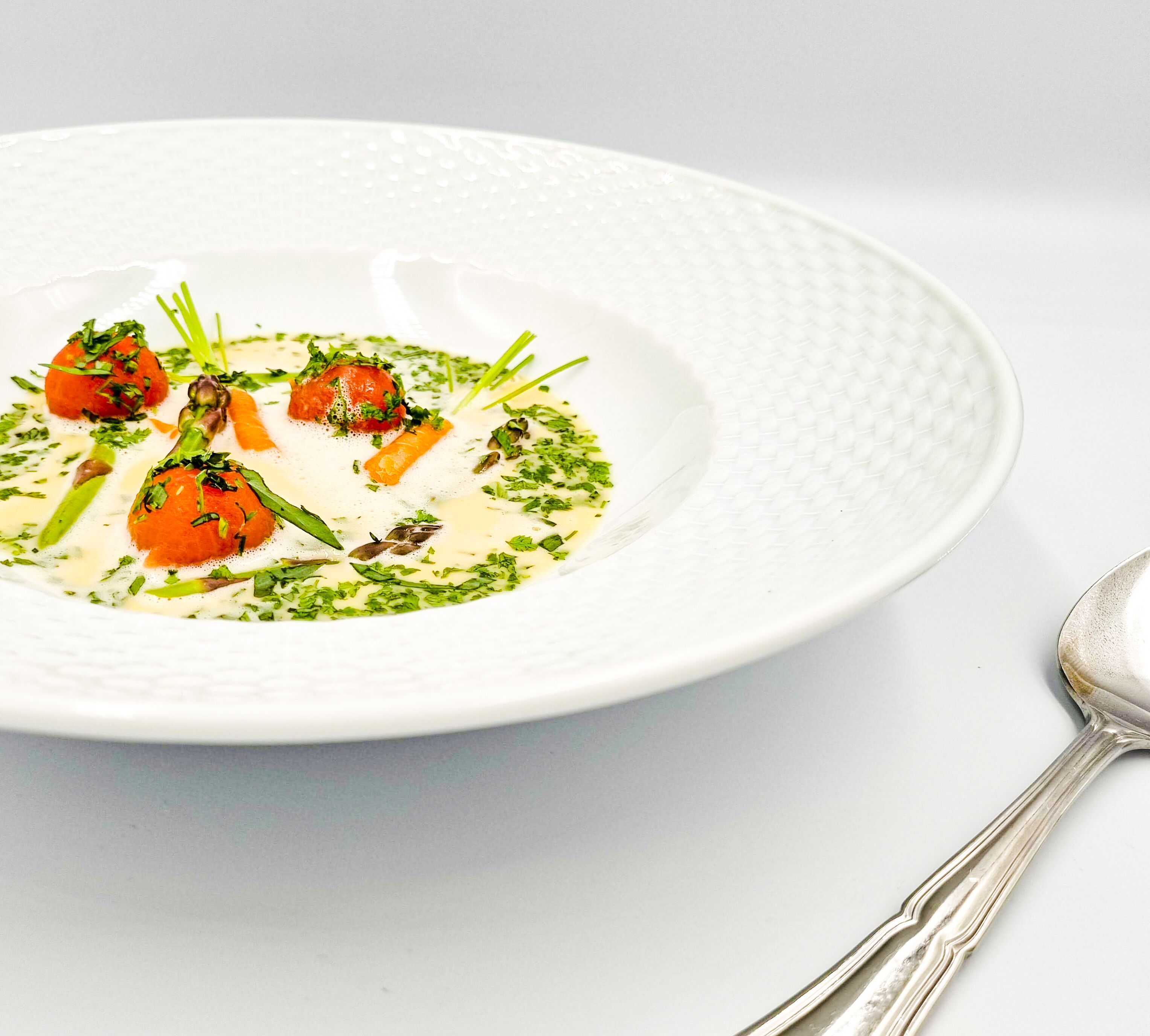 Un plato blanco con crema de sopa decorada con hierbas y verduras, acompañado de una cuchara.