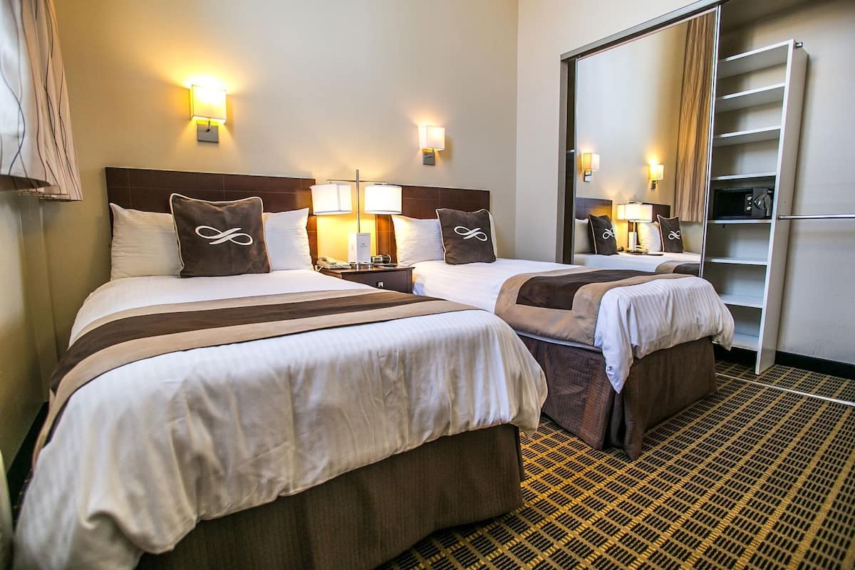A hotel room with two beds, bedside lamps, a mirror, and a wardrobe.