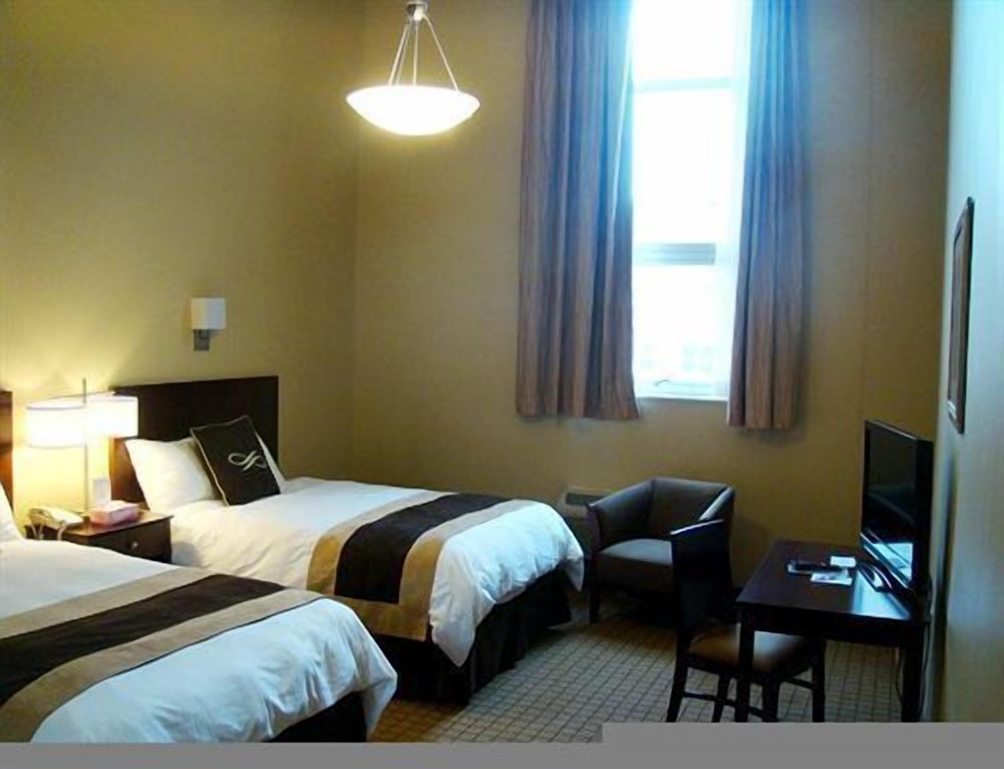 Une chambre d’hôtel avec deux lits, un bureau, une chaise, une télévision et une fenêtre avec des rideaux.
