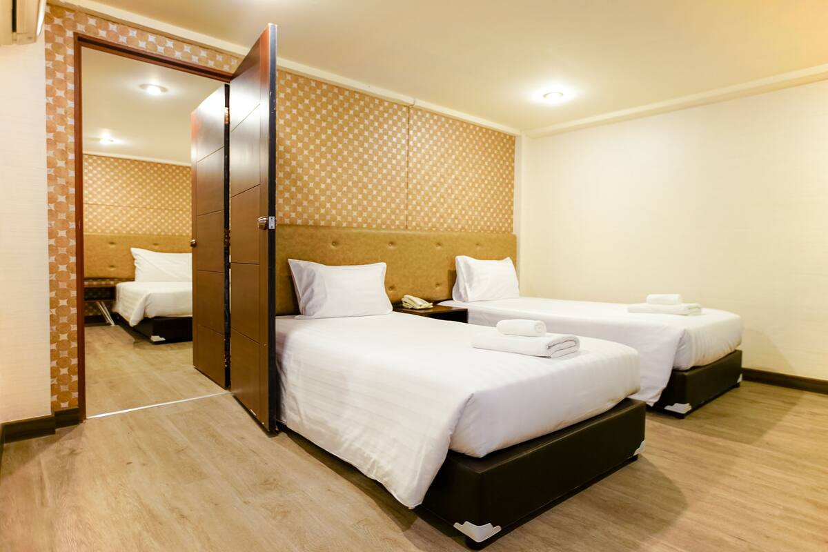 Ein Hotelzimmer mit zwei Betten, Holzboden, Wand mit Muster und einem Spiegel.