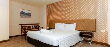 A neatly arranged hotel room with a large bed, a wooden nightstand, a desk, and a patterned wall.