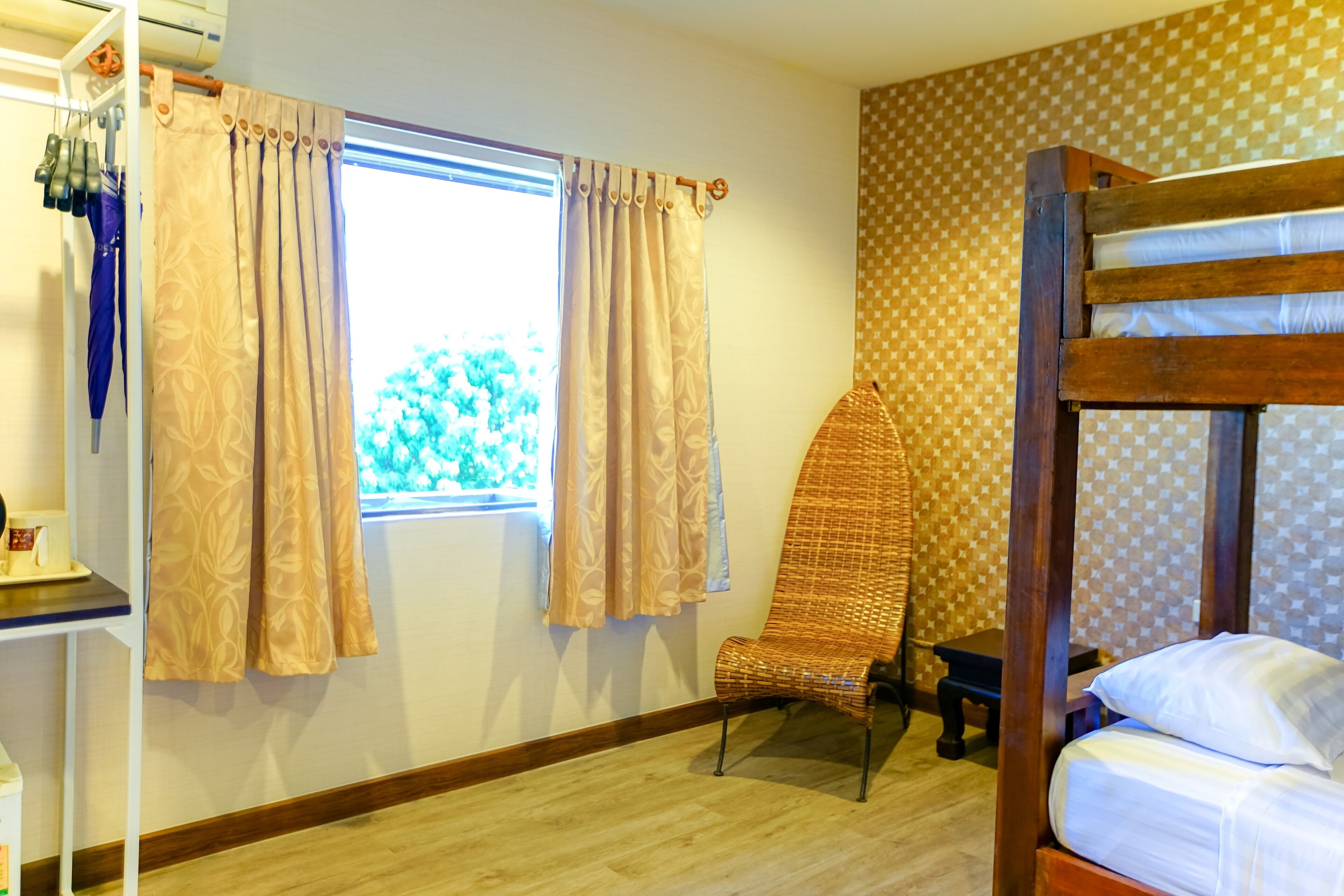 Una habitación con literas, una silla, una mesita y una ventana con cortinas.