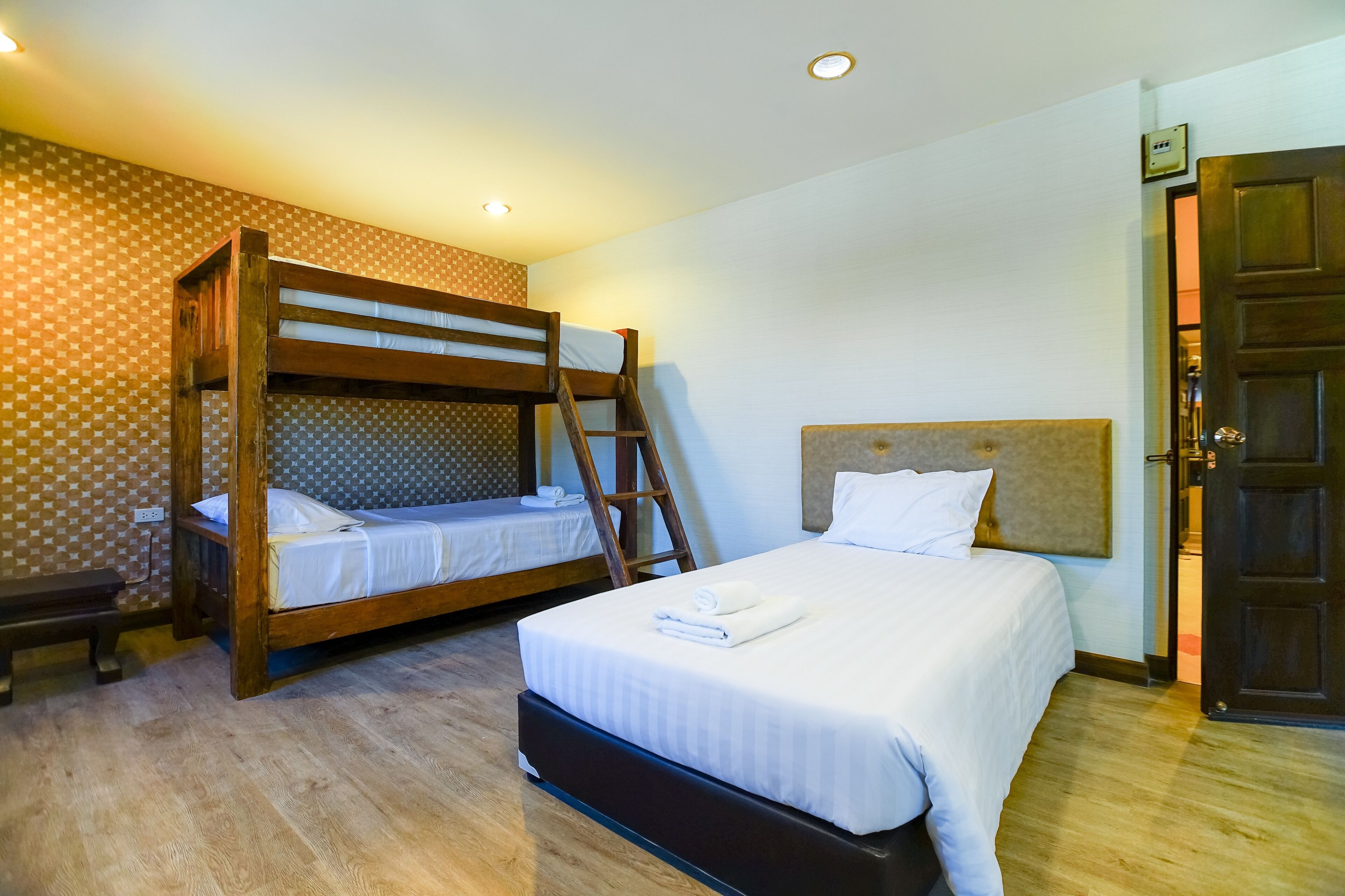 Una habitación de hotel con literas, una cama individual, suelo de madera y una puerta.