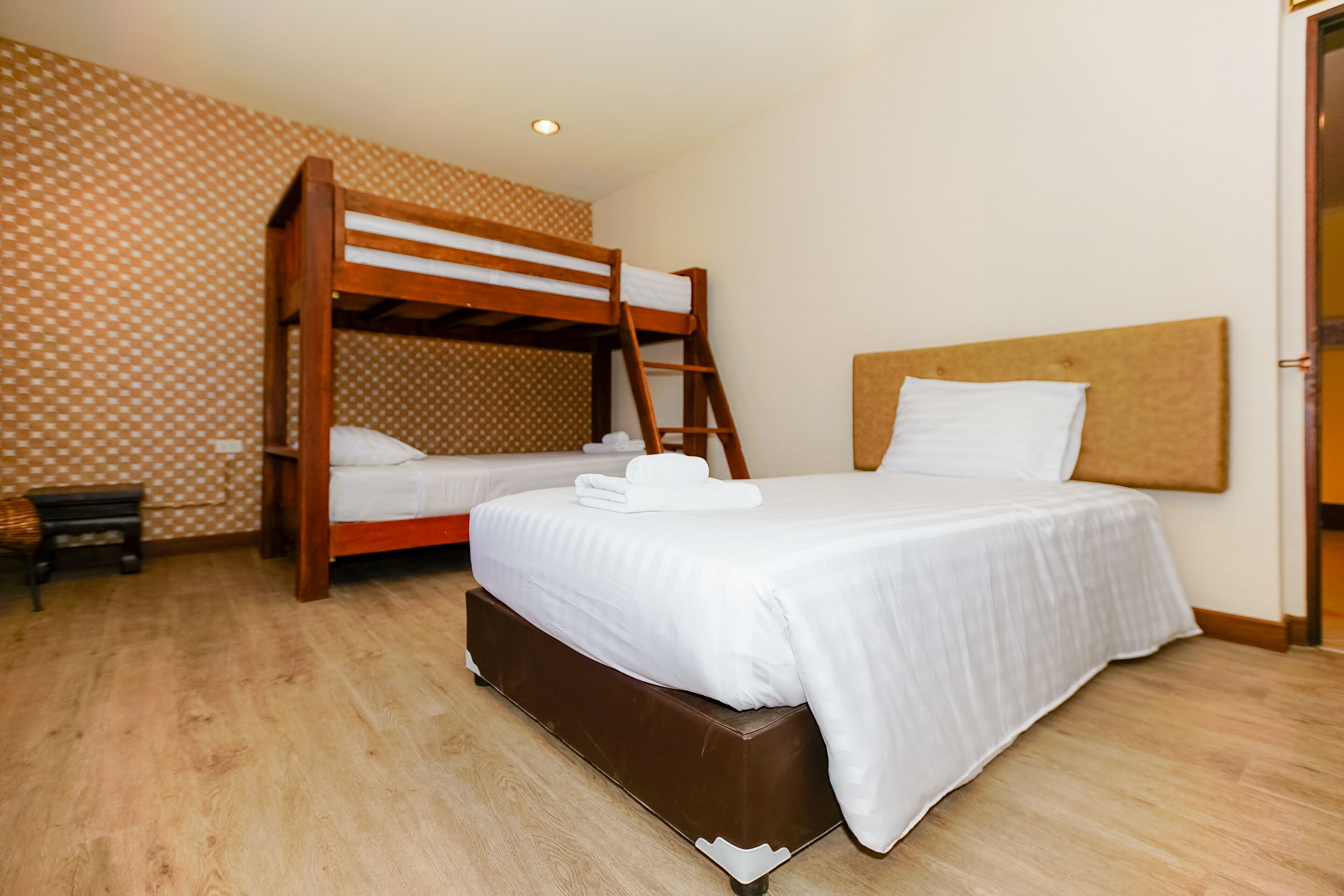 A room with two beds, one with a wooden bunk and the other with a headboard.