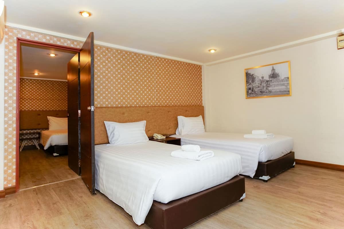 Ein Hotelzimmer mit zwei Betten, Holzboden, einem gemusterten Wandbild und einem gerahmten Bild.