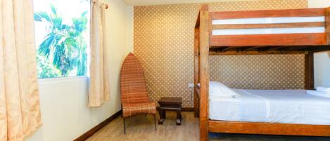 A room with a bunk bed, a small wooden table, a chair, and a window with curtains.