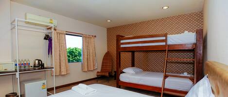 A room with a bunk bed, a single bed, a desk with a computer, a small fridge, and a window with curtains.