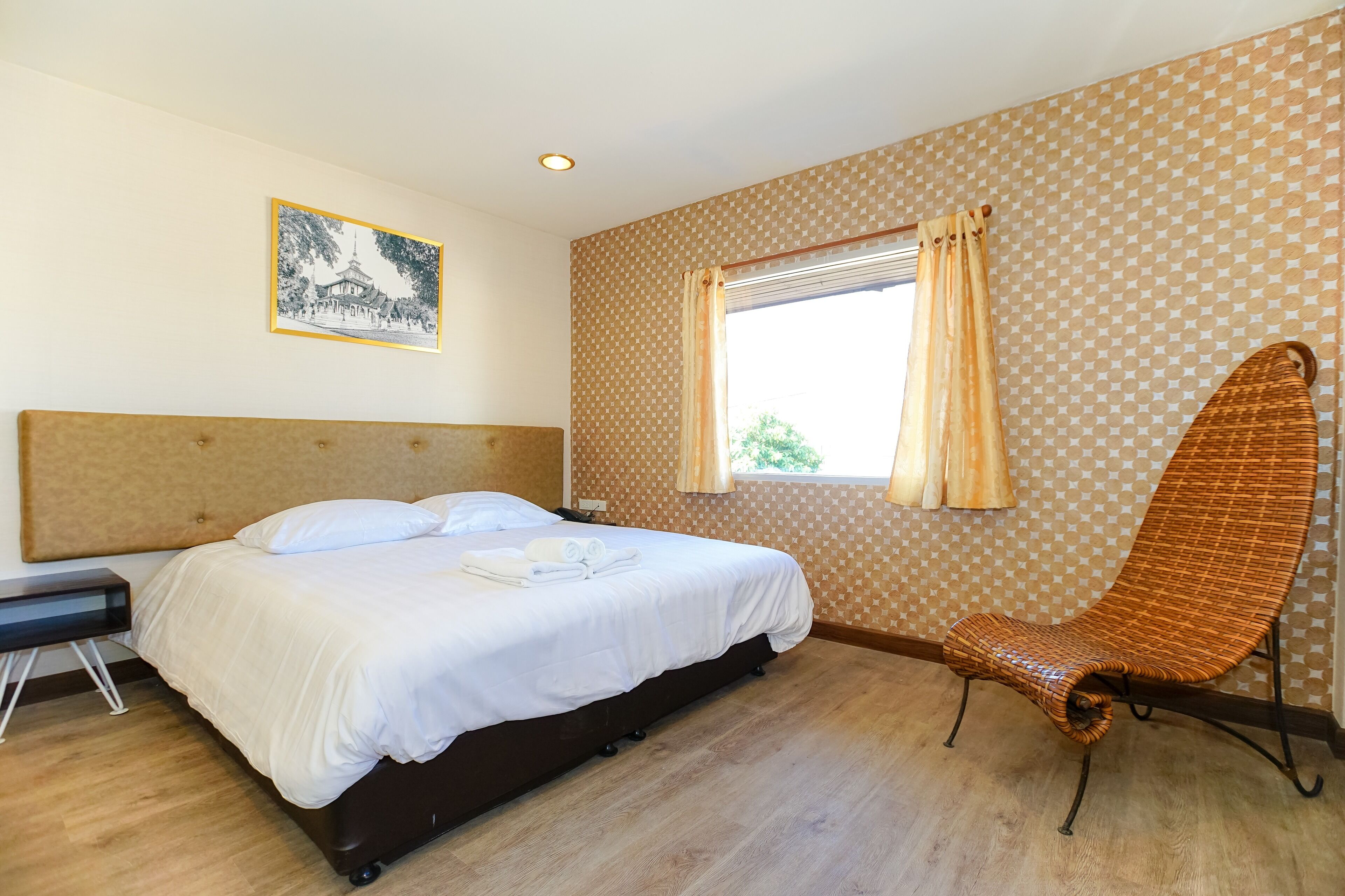 A bedroom with a bed, a chair, a bedside table, and a window with curtains.