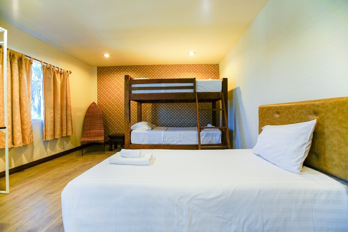 Une chambre avec un lit superposé, un lit simple, une chaise et une fenêtre avec des rideaux.