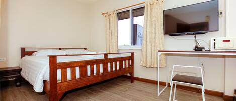 Un dormitorio con una cama de madera, un escritorio con una silla, un televisor y un equipo de aire acondicionado.