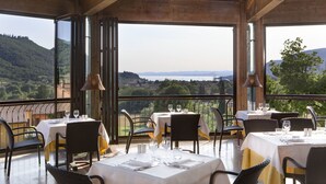 Een restaurant met gedekte tafels, grote ramen met uitzicht op berglandschap en houten balken in het plafond.