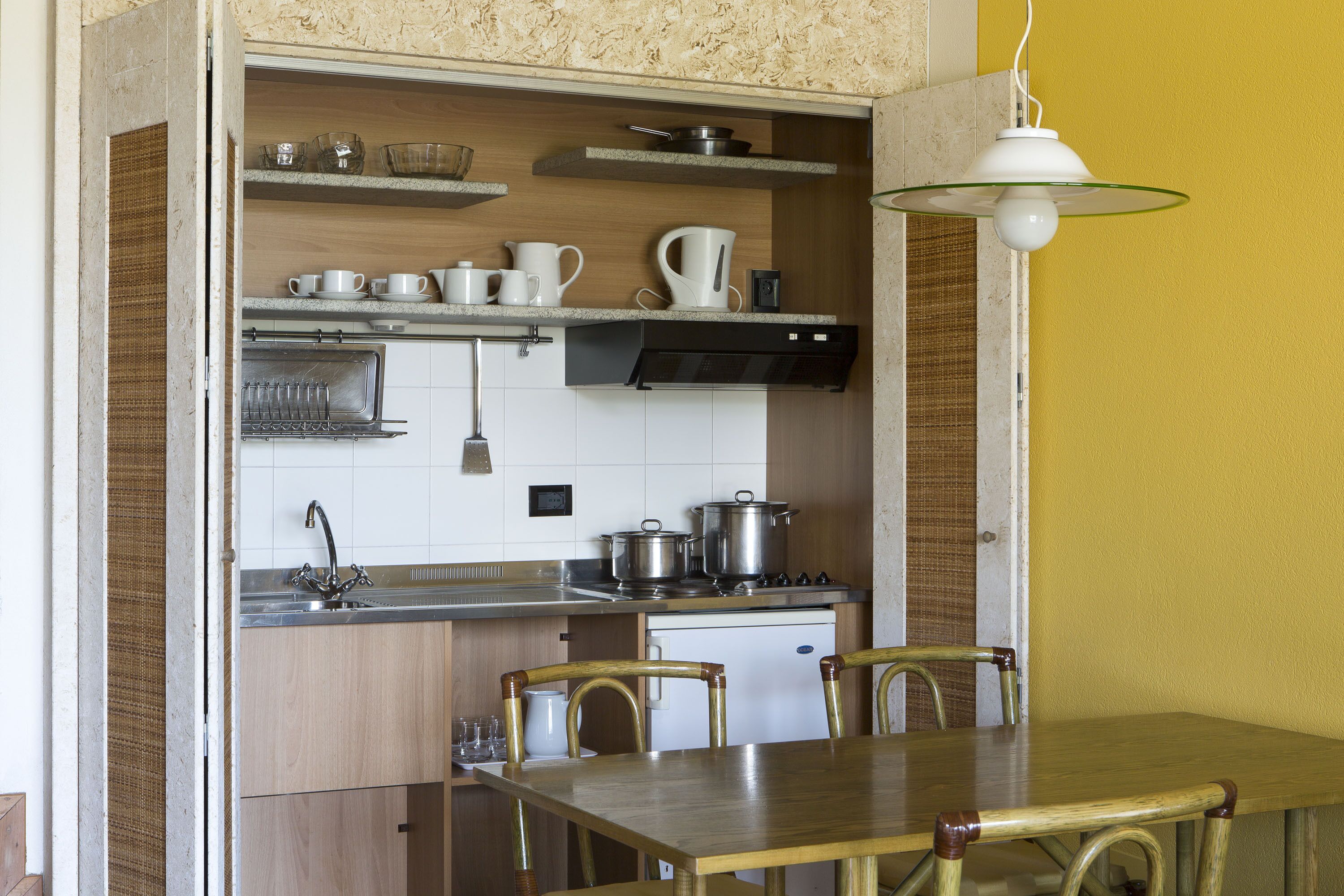 A compact kitchen with a dining area, featuring a wooden table, chairs, a sink, and a stove.