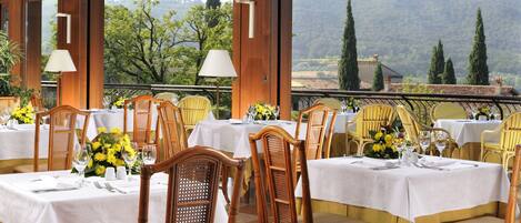 A restaurant with tables set for dining, wooden chairs, and a view of the mountains.