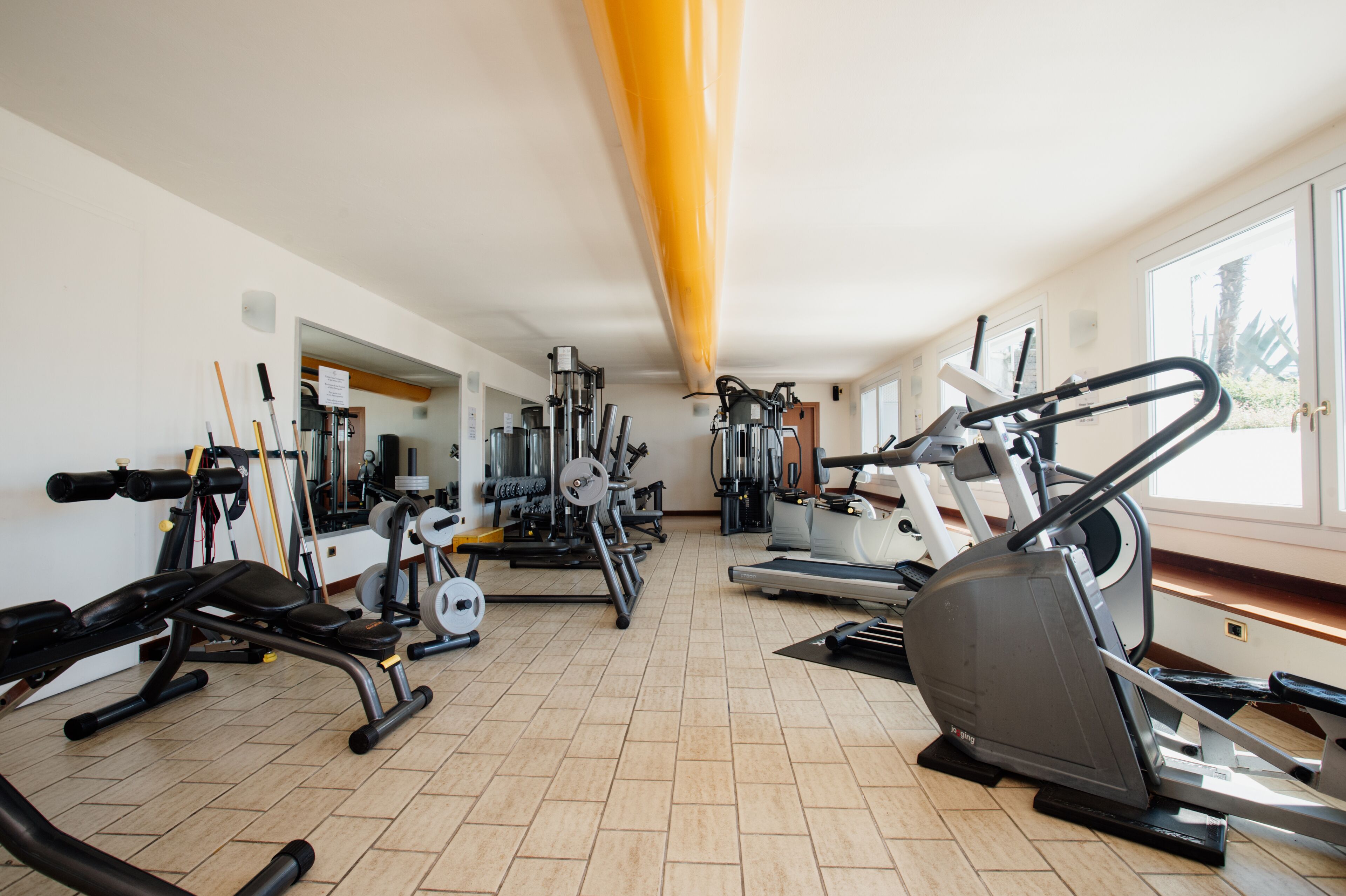 A gym with various exercise equipment, including treadmills and weight machines, arranged in a spacious room with large windows.