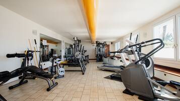 Un gimnasio con diversos equipos de ejercicio, incluyendo cintas de correr y máquinas de pesas, dispuesto en una sala amplia con ventanas grandes.