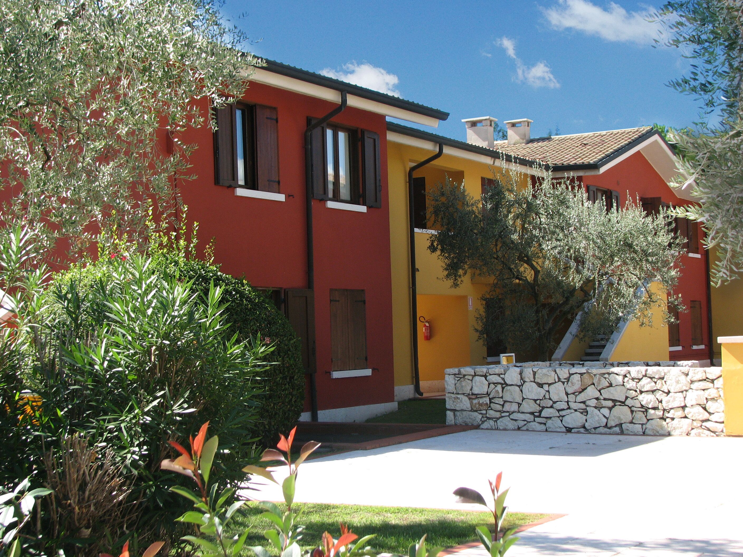A two-story building with a red and yellow facade, stone steps, and a stone wall.