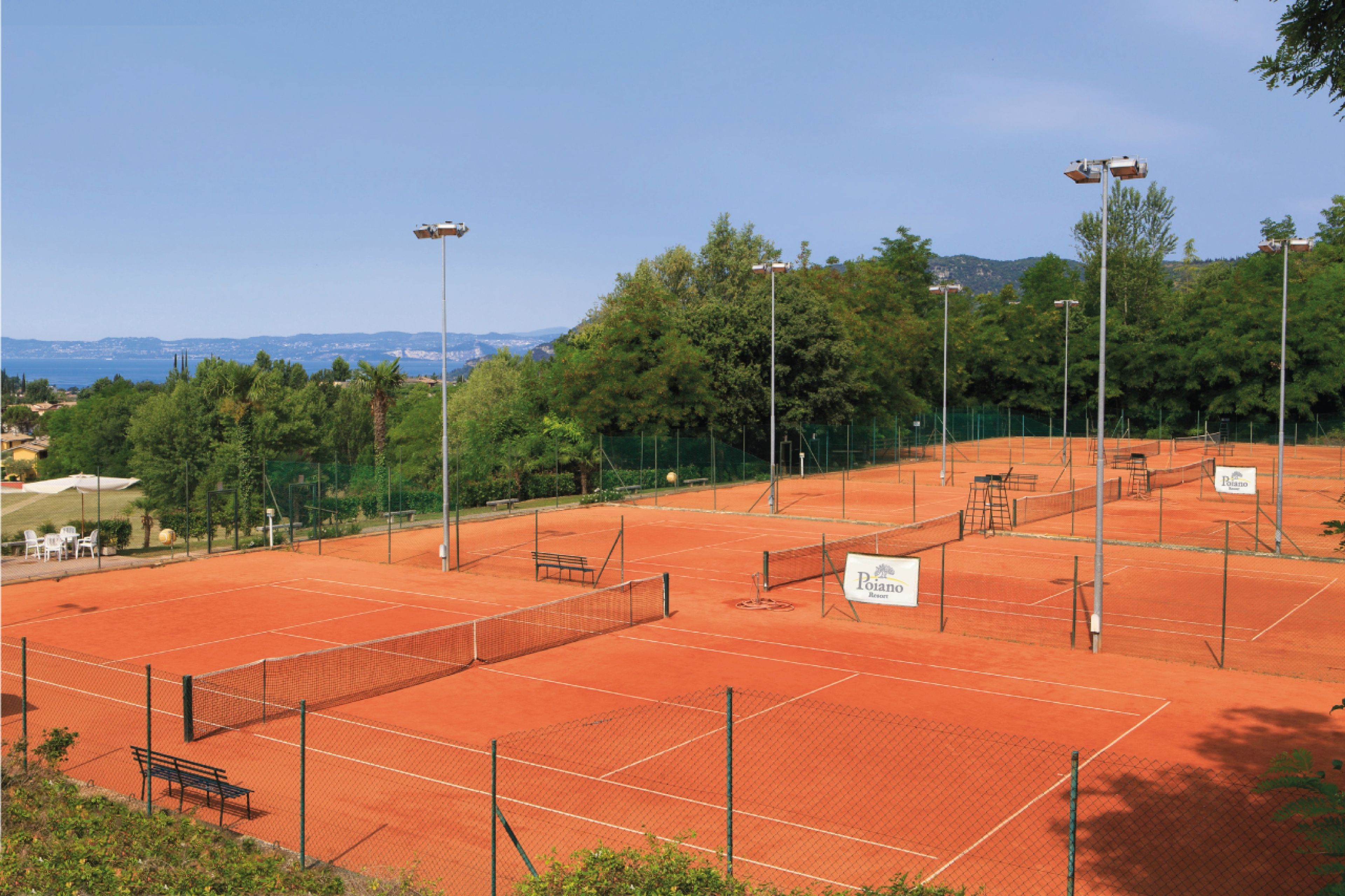 Una cancha de tenis con una banca, un cartel y una valla.
