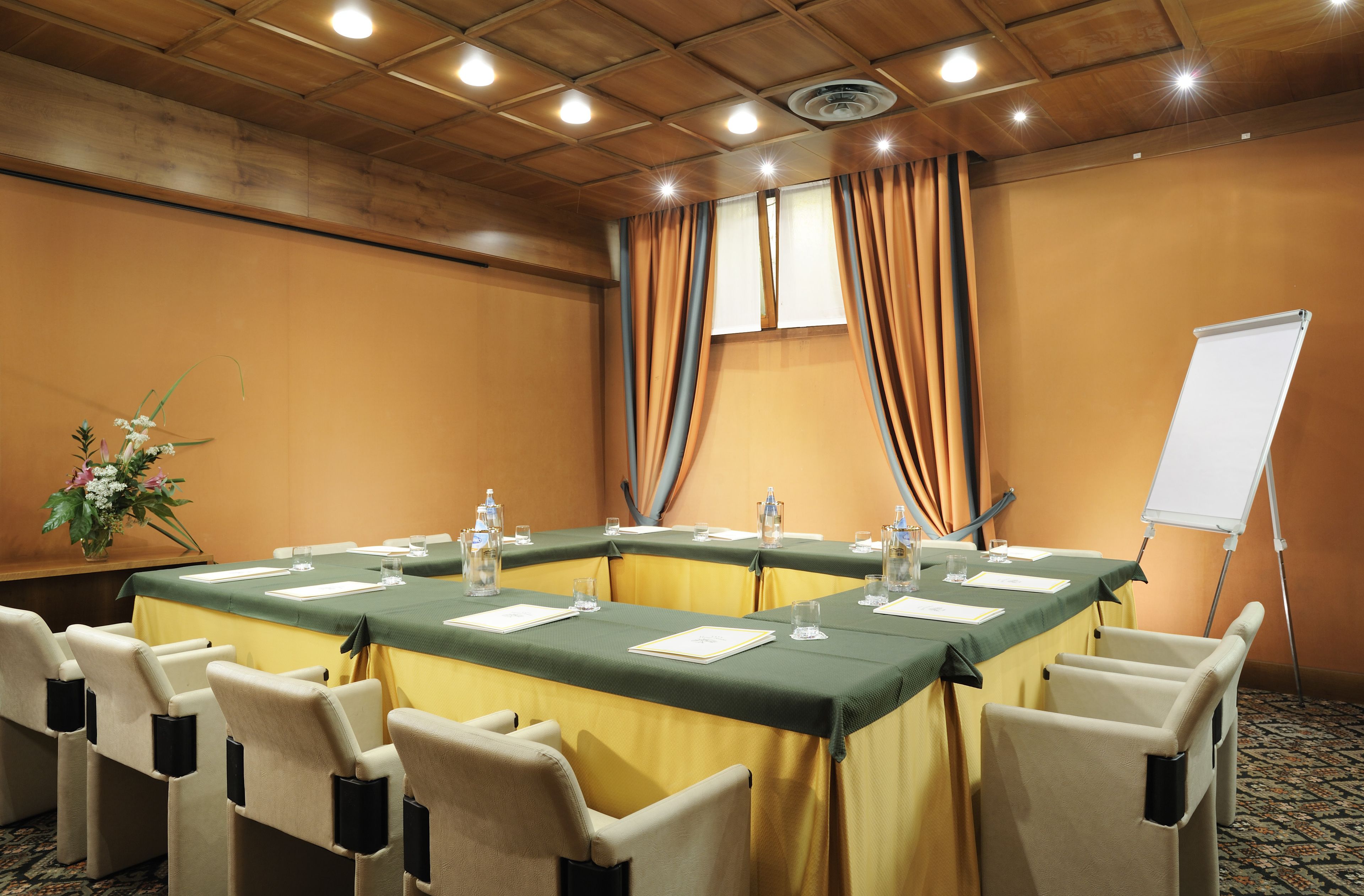 A conference room with a long table, chairs, a whiteboard, and a floral arrangement.