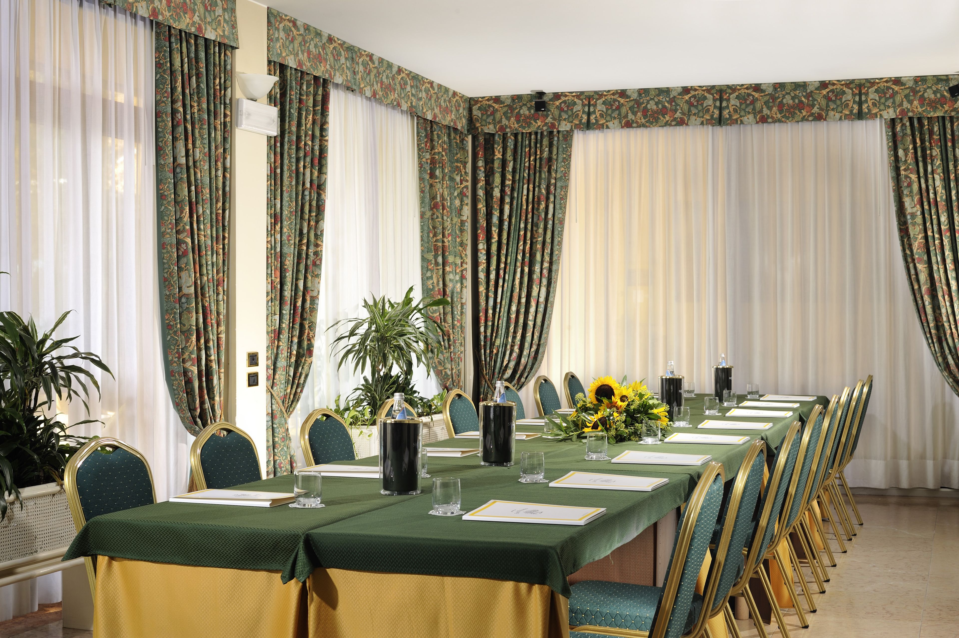 Une salle de conférence avec une longue table préparée pour une réunion, entourée de chaises et agrémentée de compositions florales et de bougies.
