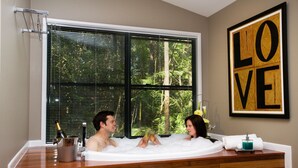 A couple in a hot tub with a view of trees through the window, a wooden counter, and a 'LOVE' artwork on the wall. - Amore On Buderim Luxury Rainforest Cabins (Buderim)