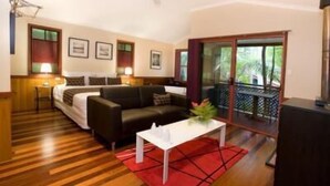 A hotel room with a wooden floor, a black sofa, a white coffee table, and a balcony with a view of greenery. - Amore On Buderim Luxury Rainforest Cabins (Buderim)