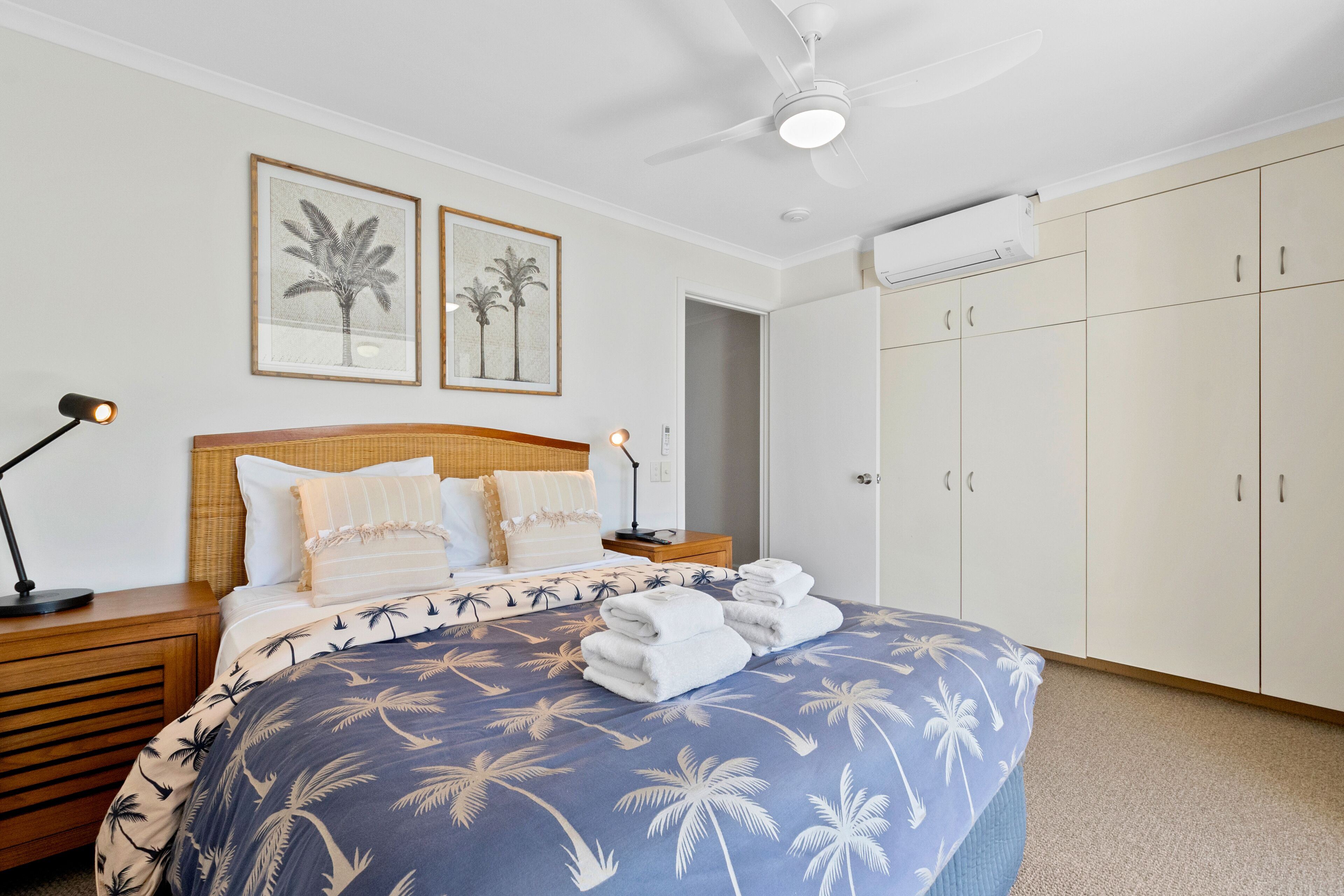 Une chambre à coucher comprenant un lit, une table de chevet, un ventilateur de plafond et une armoire.
