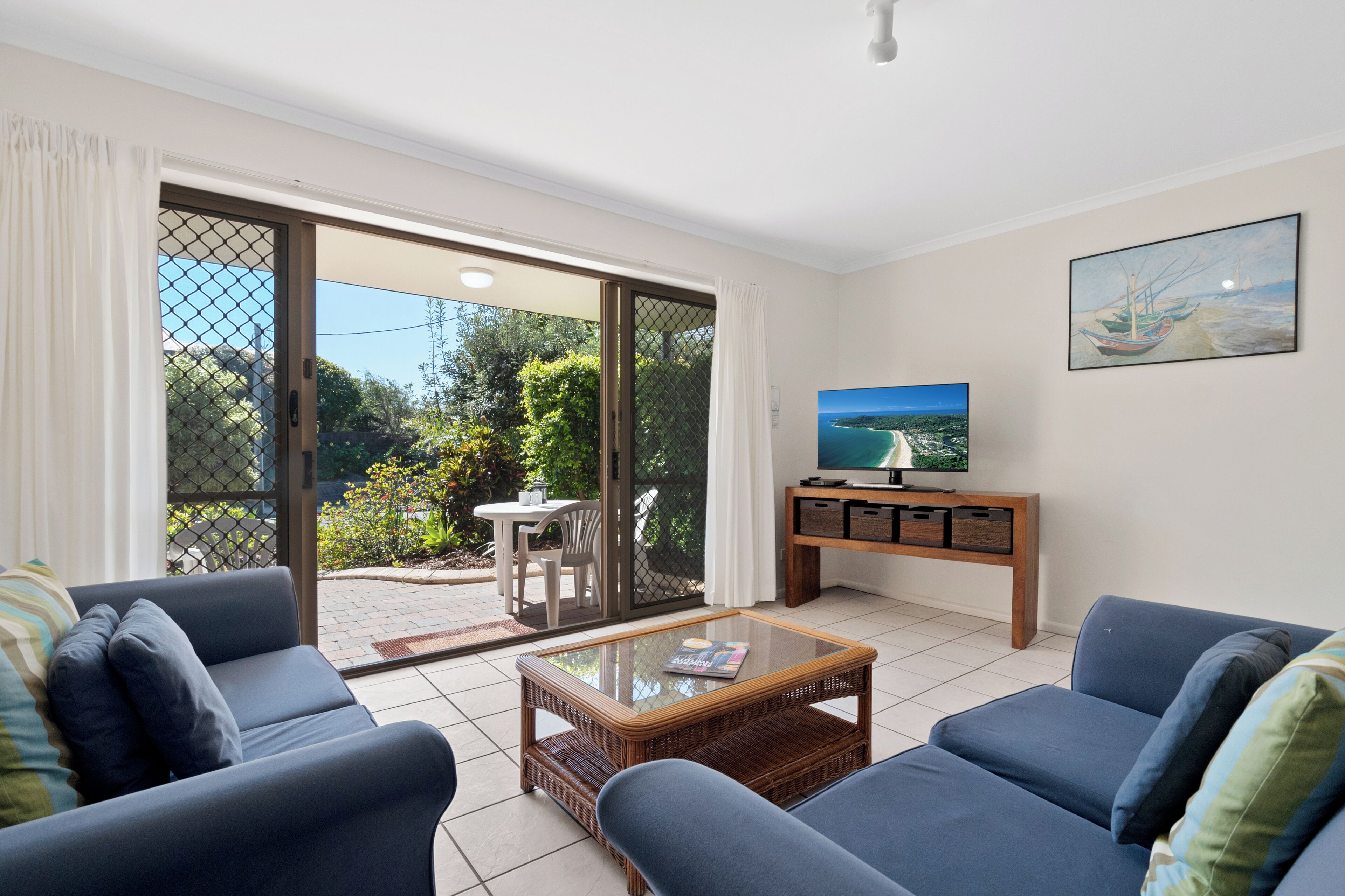 A living room with a sofa set, a coffee table, a TV, and a sliding glass door leading to an outdoor area with a table and chairs.