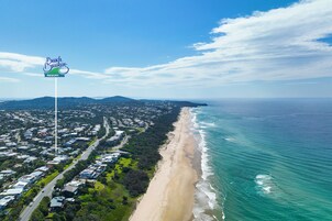 Vista aérea de una zona costera con una playa, un cartel de Beach Breakers Resort y una combinación de edificios residenciales y comerciales.