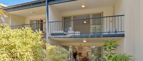 A two-story residential building with a balcony, a dining area, and a kitchen visible through the glass doors.