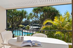 Un balcón con vista a una piscina, rodeado de palmeras y sillas de descanso.