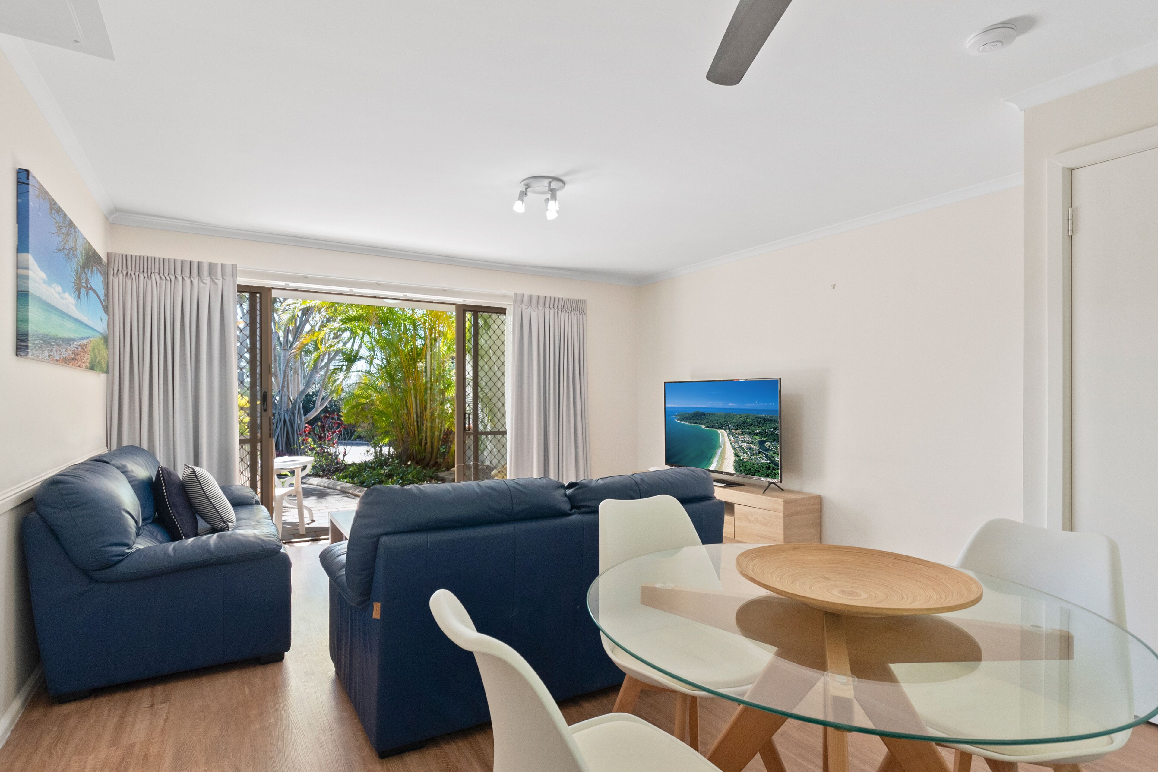 A modern living room with a sofa, a glass dining table, and a TV.