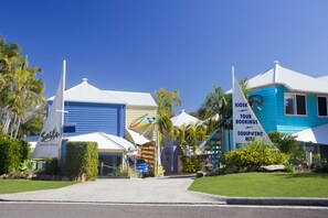 A resort with a blue building, a white tent, and a sign for tour bookings and equipment hire. - Sails Lifestyle Resort (Peregian Beach)
