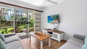 Un salon moderne avec une table en bois, un canapé gris et un téléviseur fixé au mur.