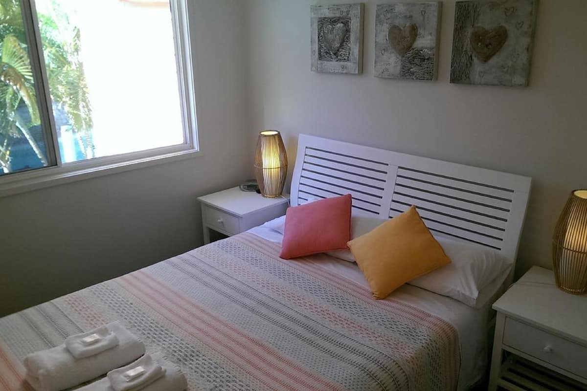 Un dormitorio ordenado con una cama, dos mesitas de noche, un ventanal y decoración en la pared.