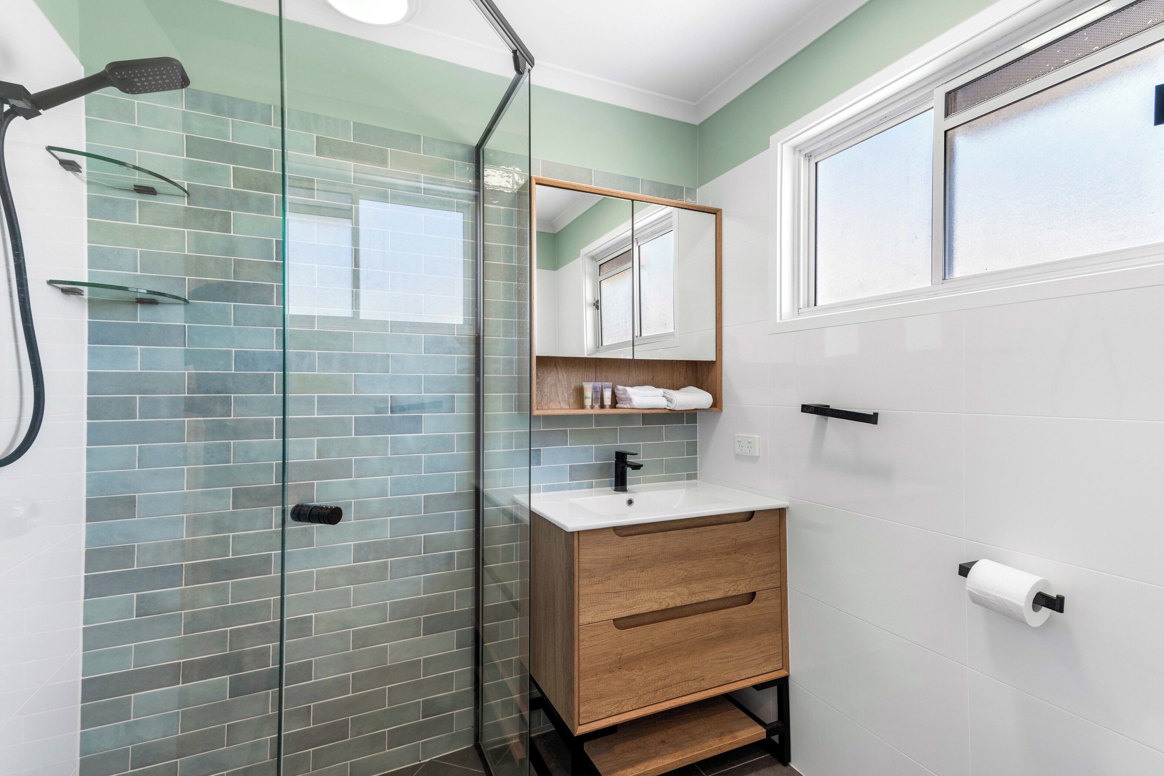 Un baño con cabina de ducha de vidrio, tocador de madera y un inodoro blanco.