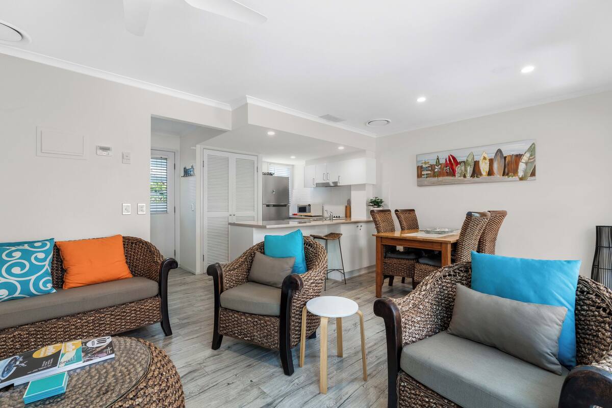Una sala moderna con muebles de mimbre, un comedor y una cocina al fondo.