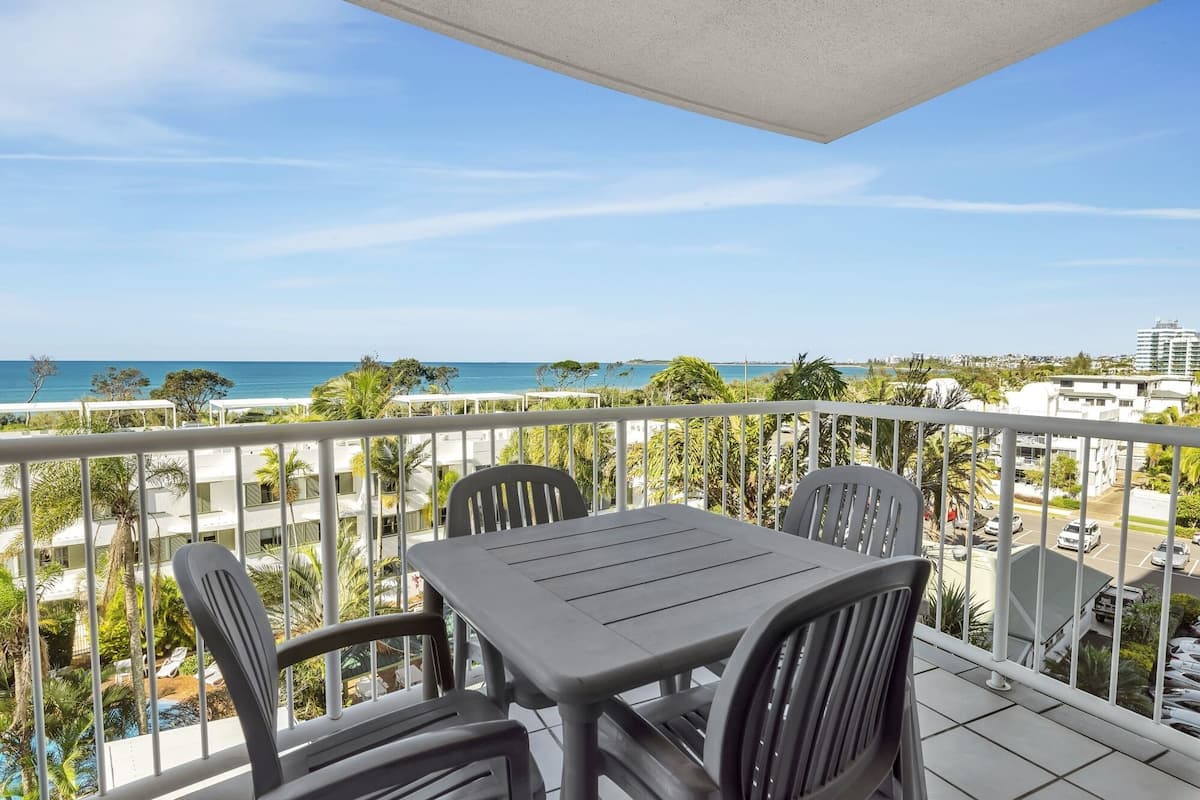 A balcony with a table and chairs overlooking a beach and cityscape.