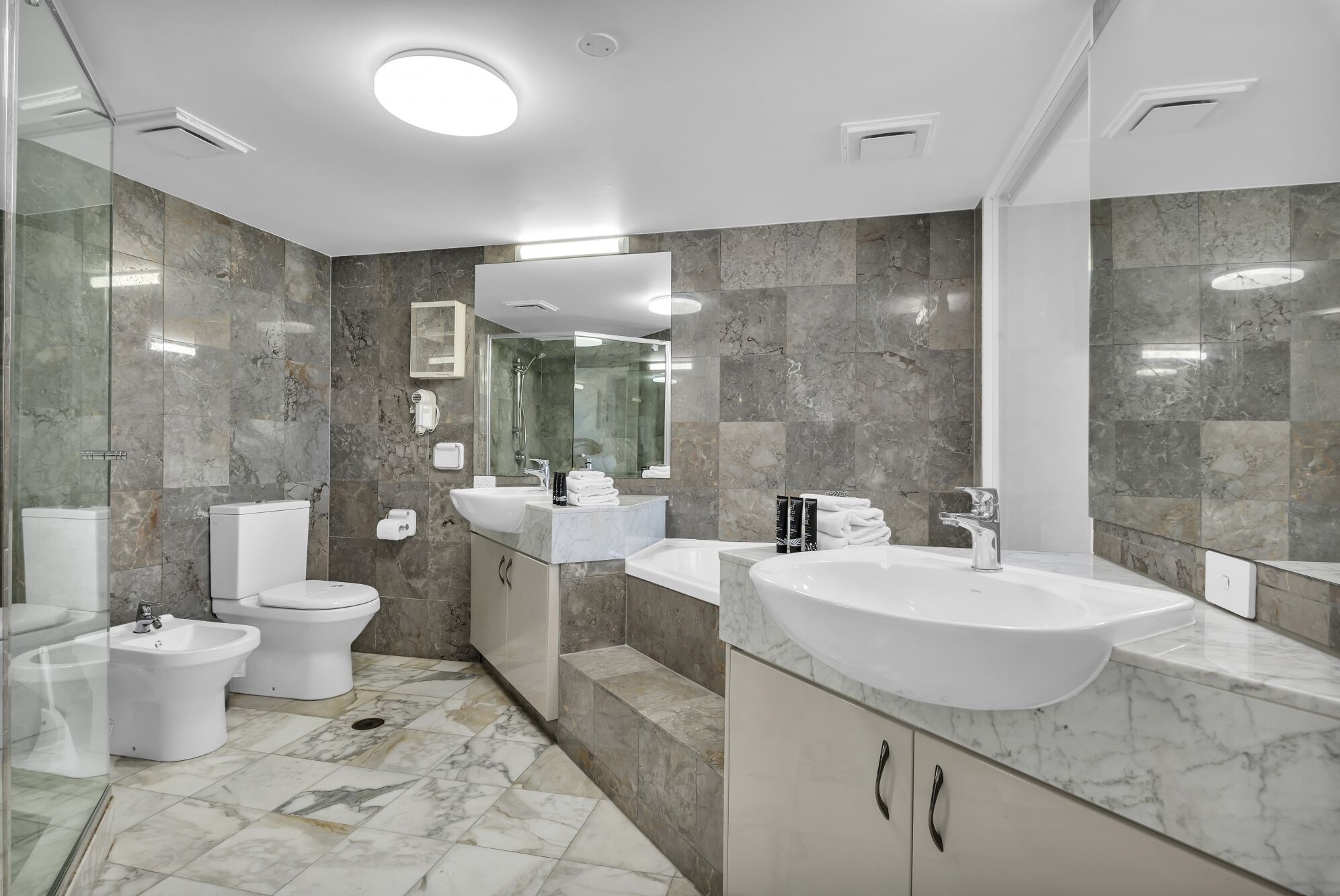 A modern bathroom with a large sink, two toilets, a bidet, and a shower.