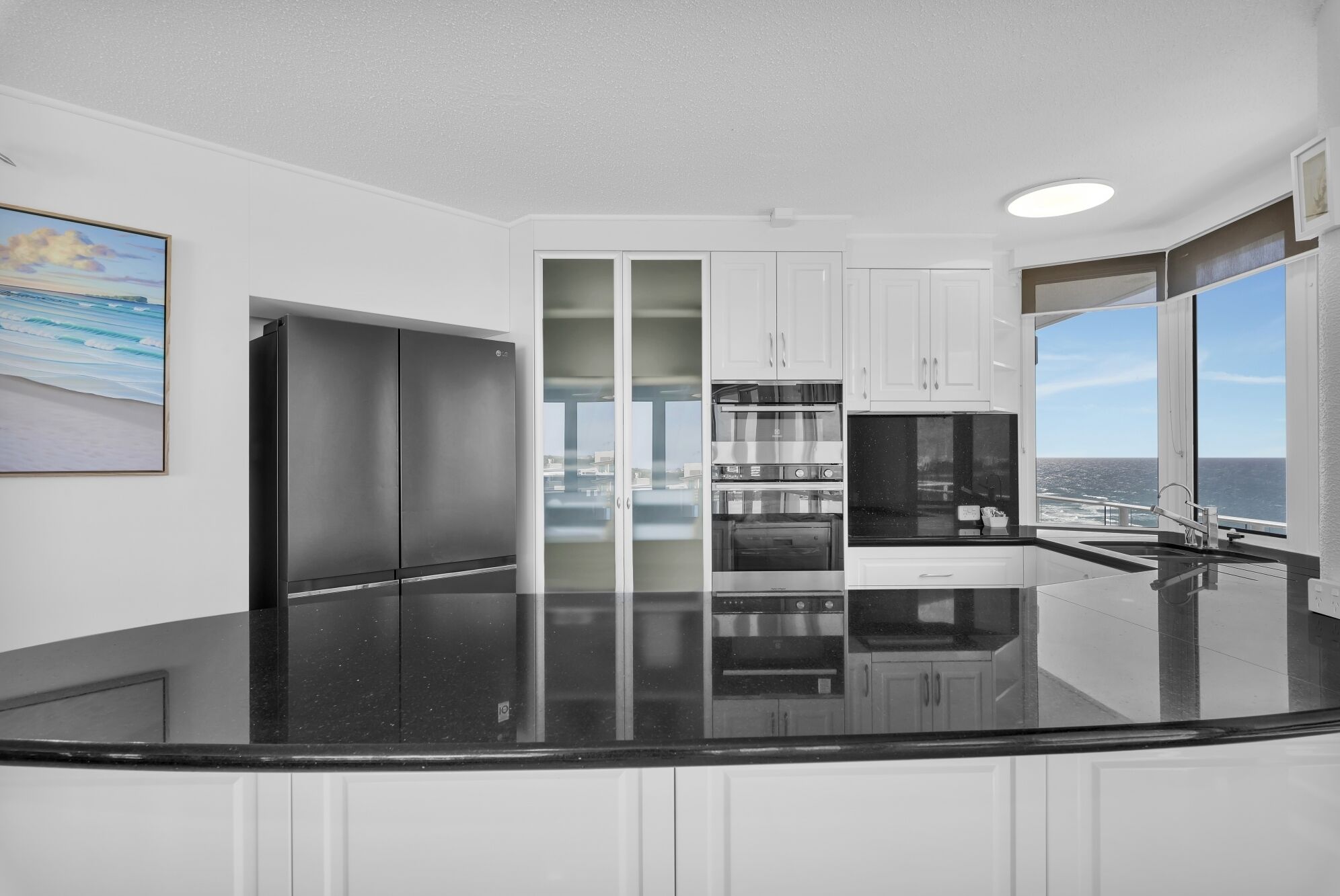 A modern kitchen with a black countertop, white cabinets, and a view of the ocean.