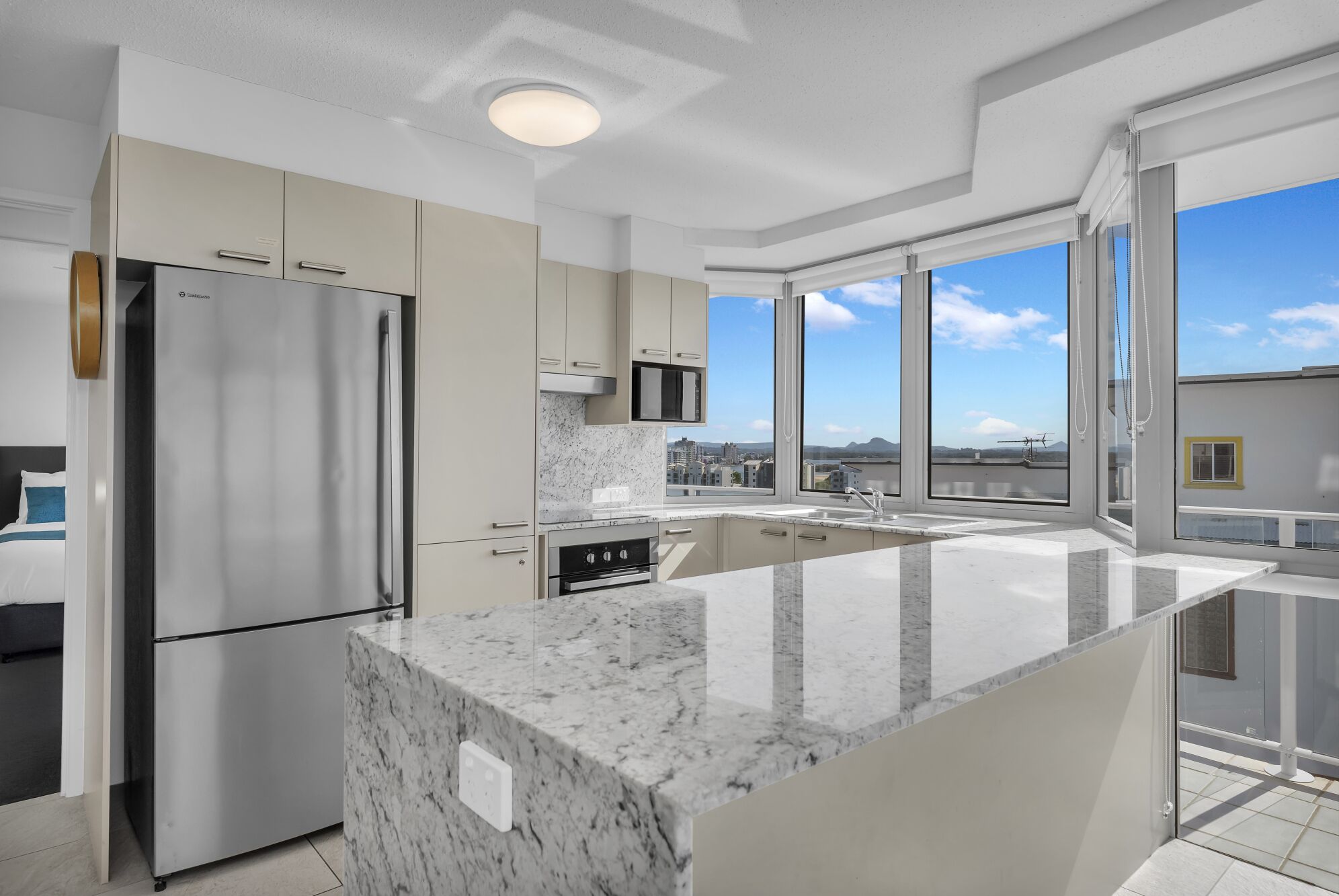 A modern kitchen with a large island, stainless steel appliances, and a city view through large windows.