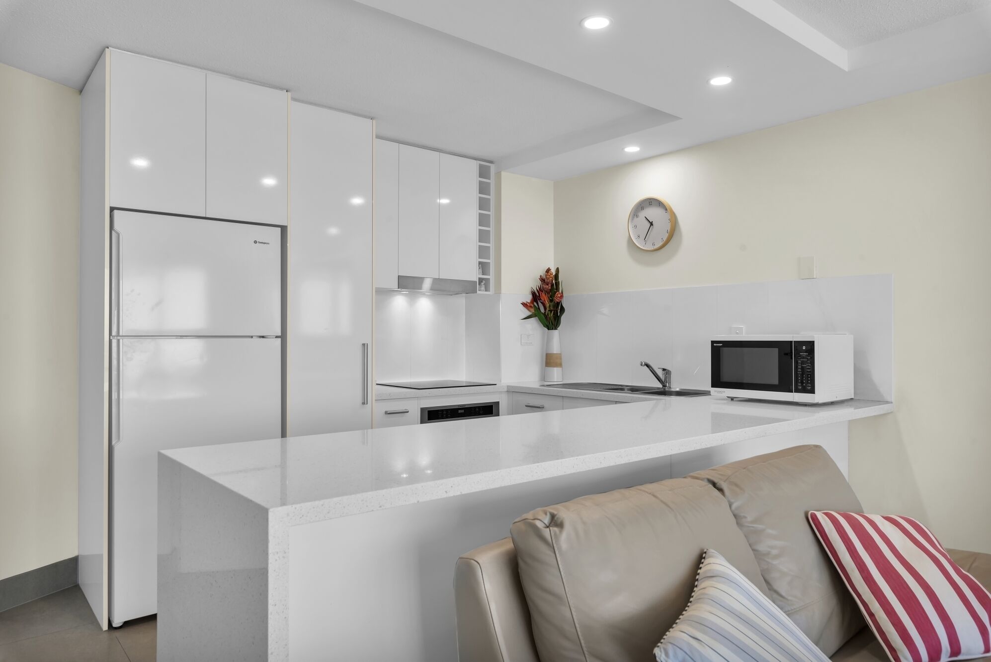 Una cocina moderna con armarios blancos, microondas integrado y un reloj en la pared.