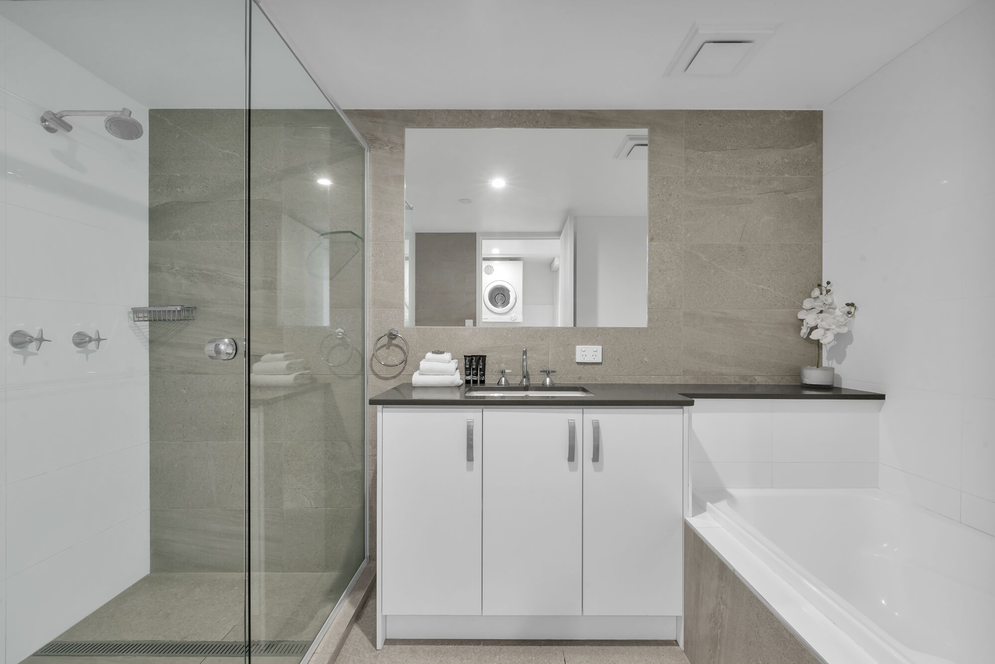 A modern bathroom with a glass shower enclosure, a sink with a mirror above, and a bathtub.