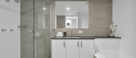 A modern bathroom with a glass shower enclosure, a sink with a mirror above, and a bathtub.