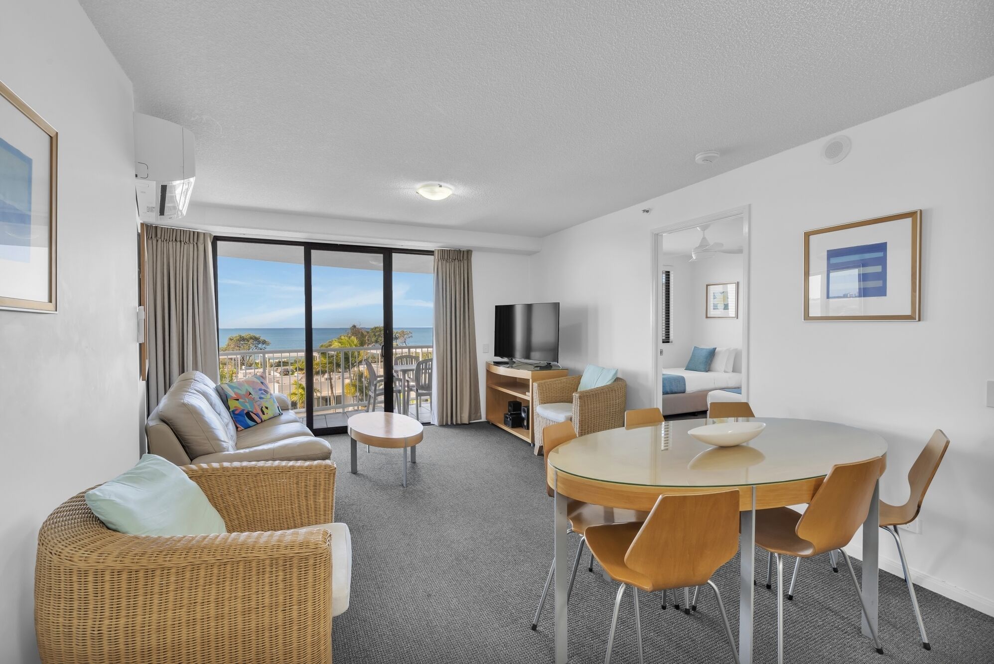 A modern hotel room with a balcony, a dining area, a sofa, and a TV.