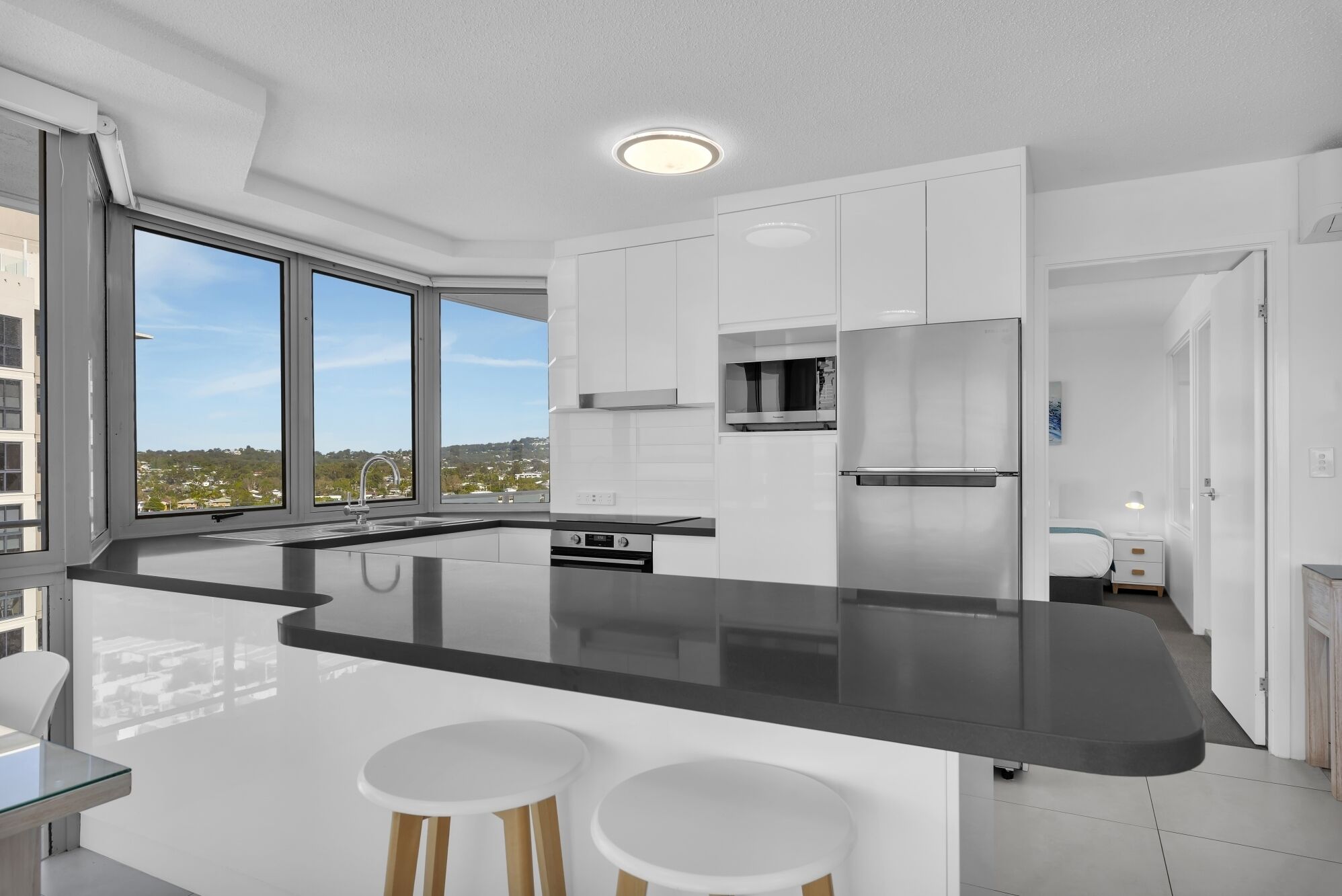 A modern kitchen with white cabinets, a black countertop, and a large window offering a city view.