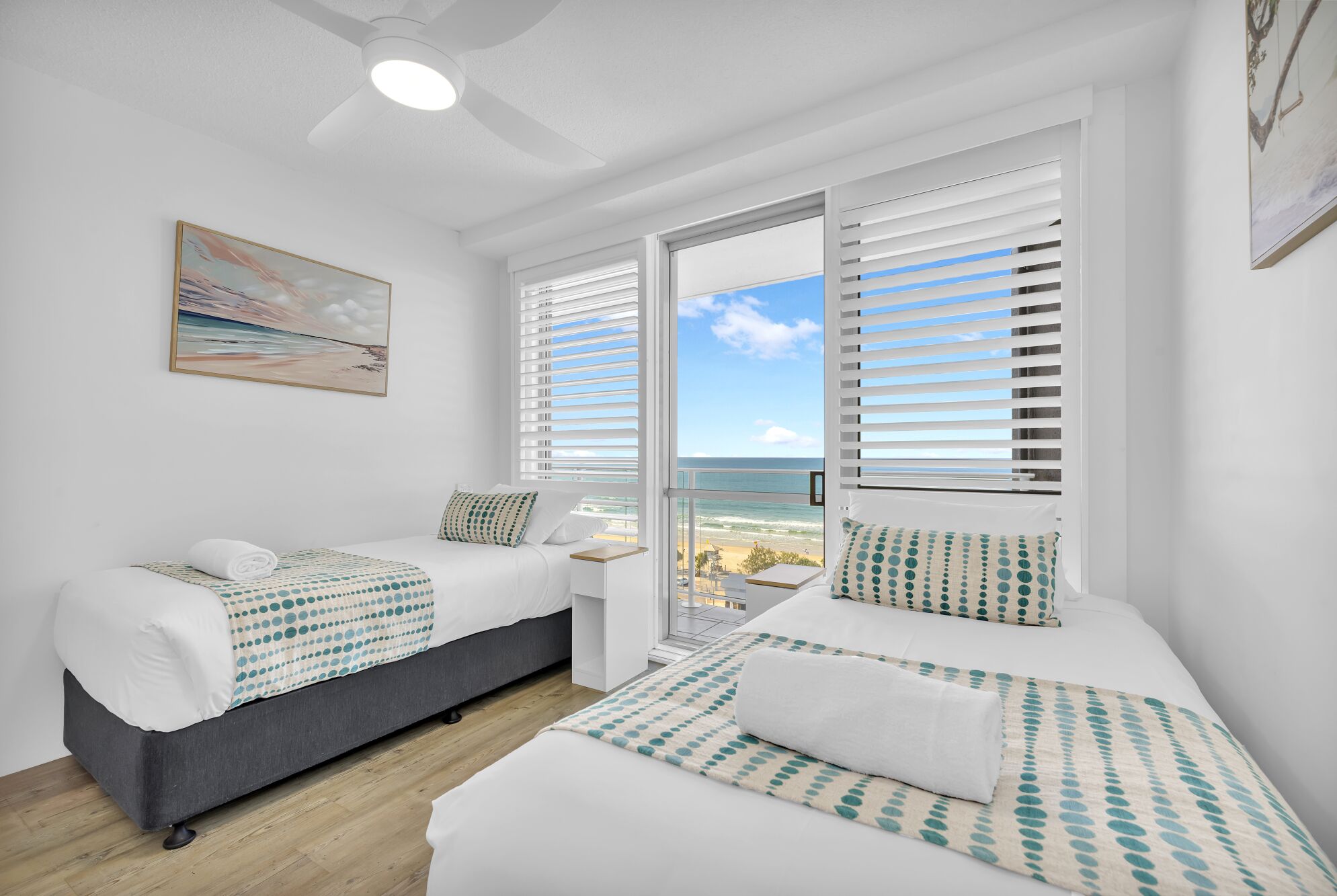 Quarto de hotel com duas camas, ventilador de teto e uma grande janela com persianas.