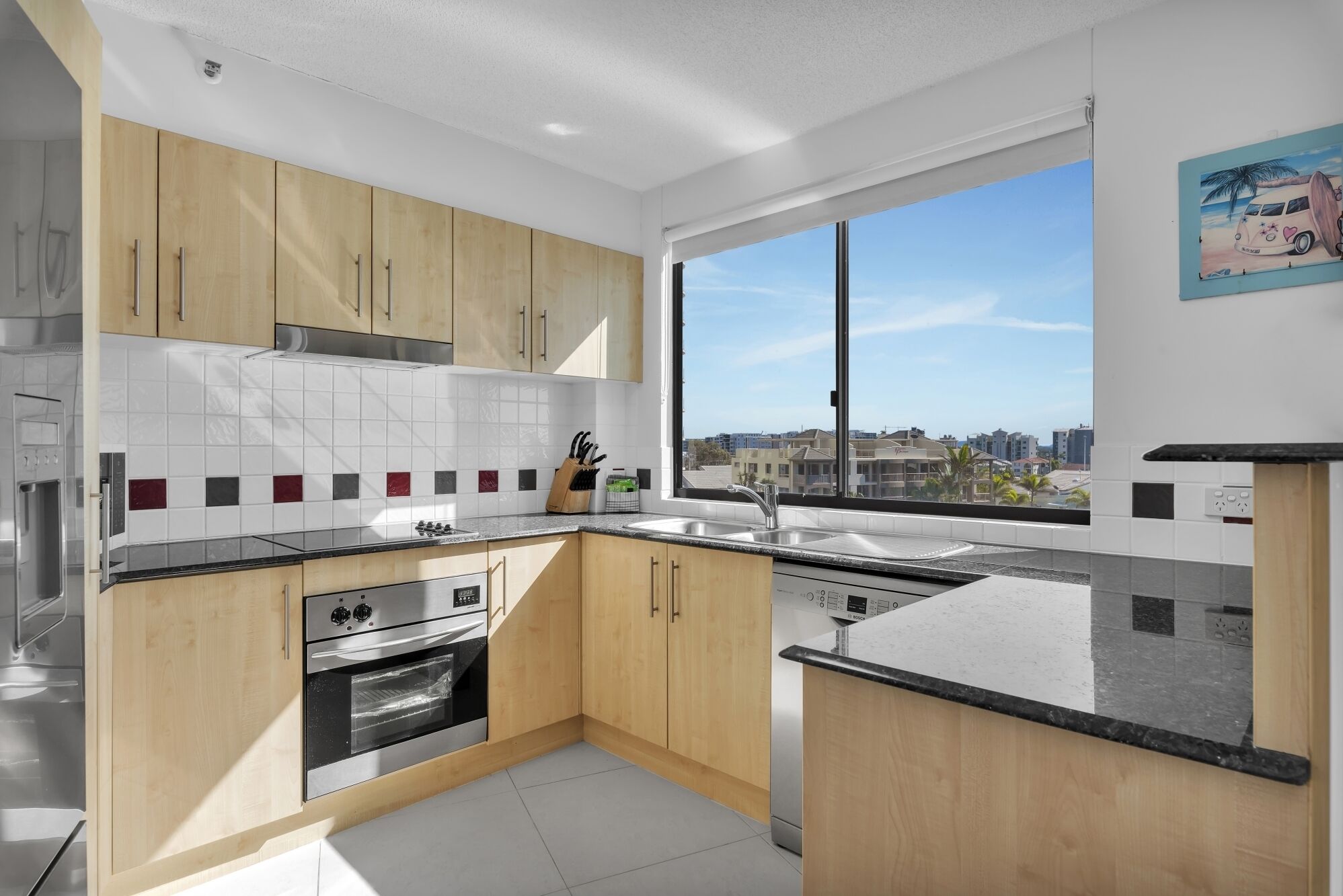 A modern kitchen with wooden cabinets, a stainless steel oven, and a large window offering a city view.
