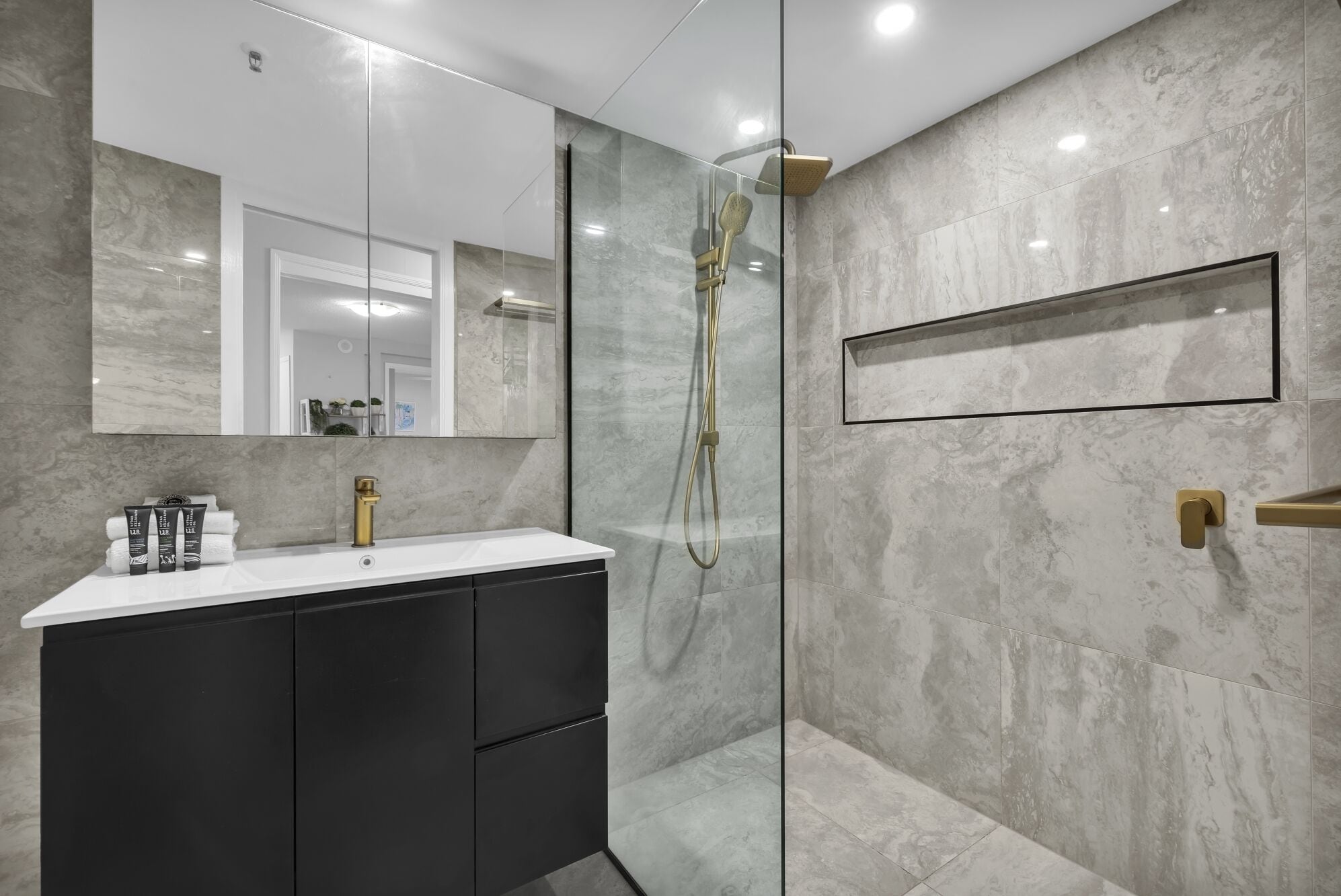 Une salle de bain moderne avec une douche à l’italienne en verre, un meuble-lavabo blanc doté de placards noirs et un grand miroir au-dessus du lavabo.