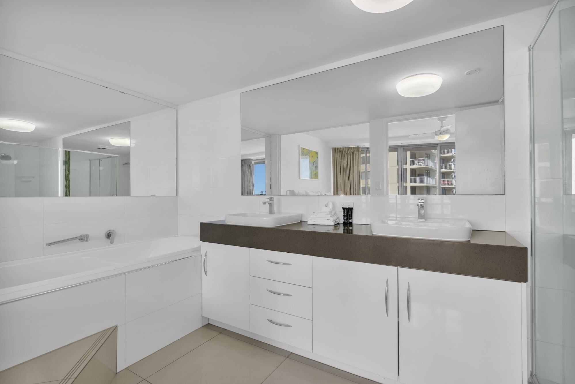 A modern bathroom with a large mirror, two sinks, and a vanity with drawers.