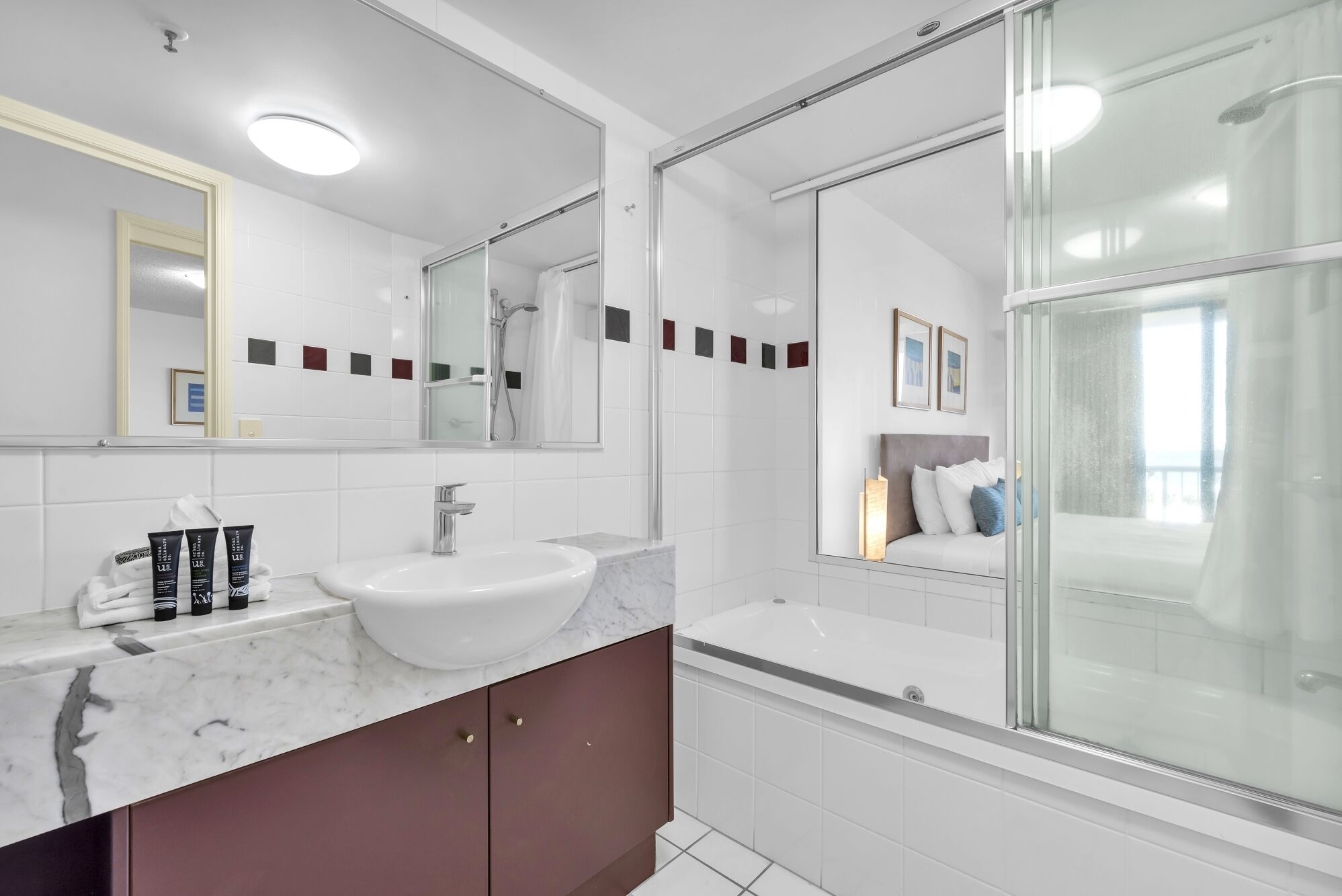 Un bany modern amb un lavabo blanc, un plat de dutxa amb envàs de vidre i un mirall gran.
